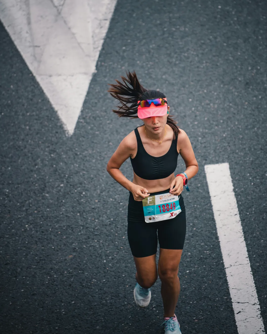 Seen from above, a runner in a race bib lands mid-stride beside a white arrow painted on the road.